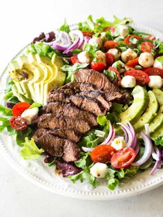 a white plate topped with steak salad and sliced avocado on top of lettuce