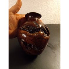 a hand holding a brown vase on top of a black table next to a white wall