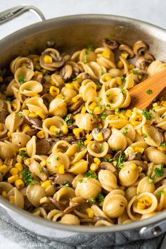 a skillet filled with pasta and mushrooms on top of a table next to a wooden spoon