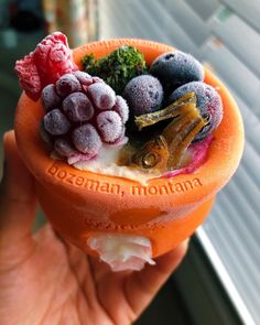 a hand holding an orange bowl filled with fruit and veggies