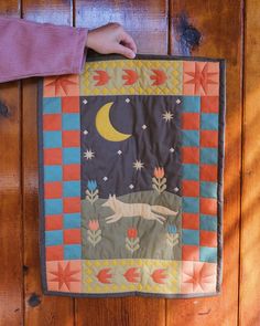 a person holding up a quilt on a wooden floor with the moon and stars above it