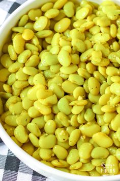 a white bowl filled with yellow beans on top of a checkered table cloth