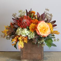 a wooden vase filled with lots of different colored flowers and greenery on top of a table