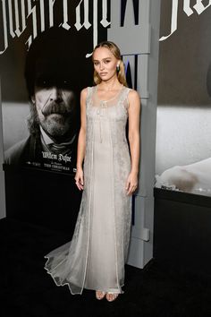 a woman standing in front of a poster at a movie event wearing a long white dress