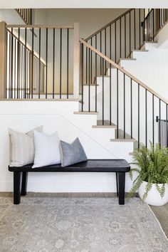 a black and white bench with pillows on it in front of a stair case next to a potted plant