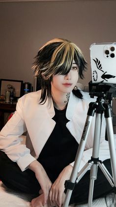 a woman sitting on top of a bed next to a tripod holding a camera