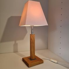 a wooden table lamp with a white shade on it's base and cord plugged in