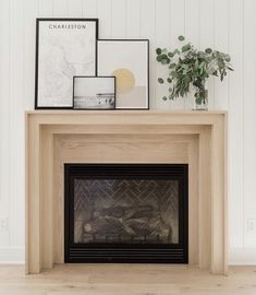 a fireplace with some pictures on top of it and a potted plant in the corner