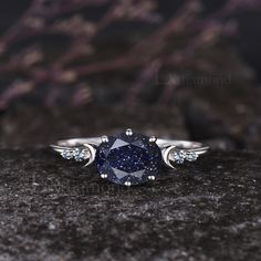 a blue diamond ring sitting on top of a black stone surface with white diamonds around it