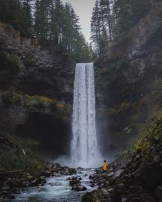 a person standing at the base of a waterfall with water coming from it's side