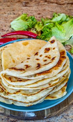 a stack of tortillas on a blue plate with lettuce and red peppers in the background