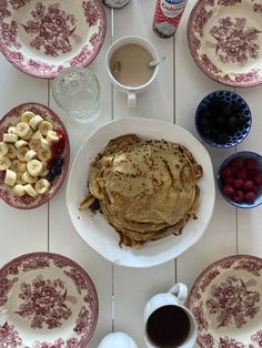 pancakes, fruit and coffee on a white table with red floral china plates in the foreground