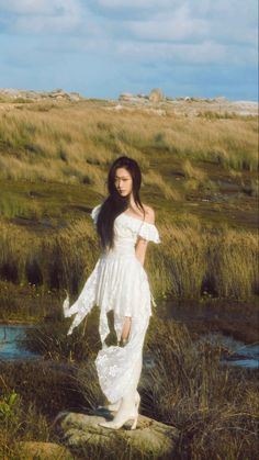 a woman in a white dress standing on a rock