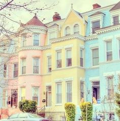 several multi - colored houses line the street with cars parked on the sidewalk in front