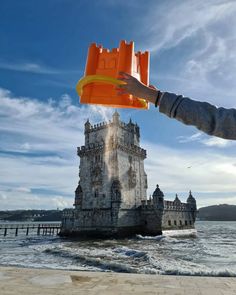 a person holding an orange object in front of a castle on the water's edge