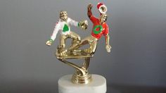 two figurines sitting on top of a white marble base with gold colored accents