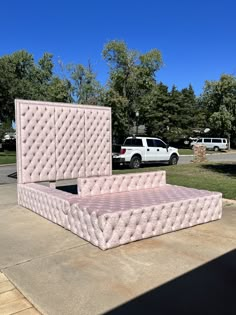 a large pink bed sitting on top of a cement slab next to a white truck