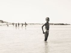 a young boy standing in the ocean with his hands on his hips and other people behind him