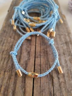 two blue rope bracelets on top of a wooden plank with gold clasps and beads