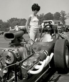 a woman standing on the back of a race car with two men looking at it