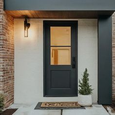 a black front door with two potted plants on the side and an entry mat