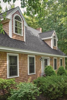 a brown house with white trim and windows in the front yard is surrounded by shrubs and trees