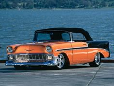 an orange classic car parked next to the water