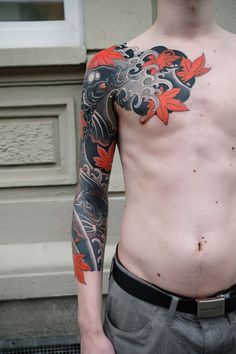 a man with a dragon tattoo on his arm and chest standing in front of a building