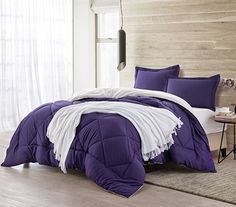 a bed with purple and white comforters in a room next to a wooden wall