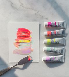 four tubes of paint next to a painting brush on a piece of paper with markers