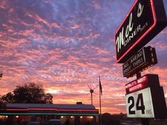 the sky is pink and purple as it sets in front of a mcdonald's