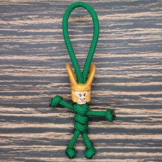 a green rope with a gold monkey head on it's end is hanging from a wooden surface