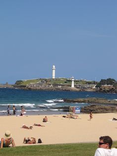 people are relaxing on the beach and in the water at this point there is a light house