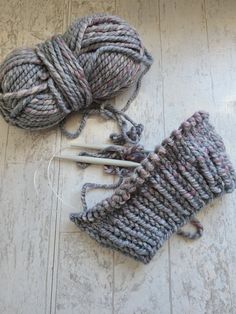 two skeins of yarn sitting on the floor next to each other with knitting needles