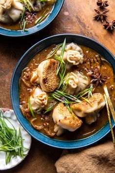 two blue bowls filled with dumplings and sauce on top of a wooden table next to an orange napkin