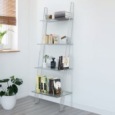 a white book shelf with books on it next to a potted plant and window