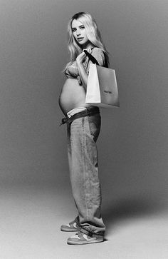 a pregnant woman holding a shopping bag in her right hand and looking at the camera