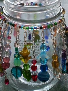 a glass jar filled with lots of different colored beads and chains hanging from it's sides