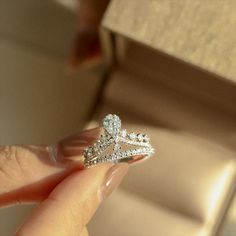 a woman's hand holding a diamond ring in front of a box with jewelry on it