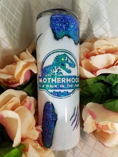 a white tumbler with blue glitter on it next to pink roses