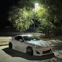 a white sports car parked in front of a street light at night with its lights on