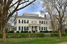 a large white house with green shutters on the front and side windows, surrounded by trees