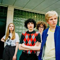 four people standing in front of a building with their arms crossed and looking at the camera