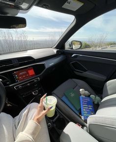 a woman sitting in the driver's seat of a car holding a cup of coffee