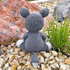 a gray crocheted teddy bear sitting on rocks