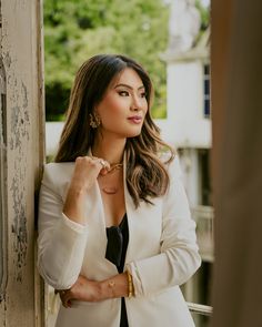 a woman leaning against a wall wearing a white jacket and black tie with her hands on her chest