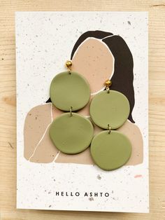 the green and beige earrings are on top of a white card that says hello asho