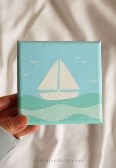 a hand holding up a small canvas with a sailboat on it