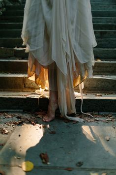 a woman in a white dress is standing on some steps with her legs crossed and there are leaves all over the ground