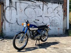 a blue motorcycle parked in front of a wall with graffiti on it's side